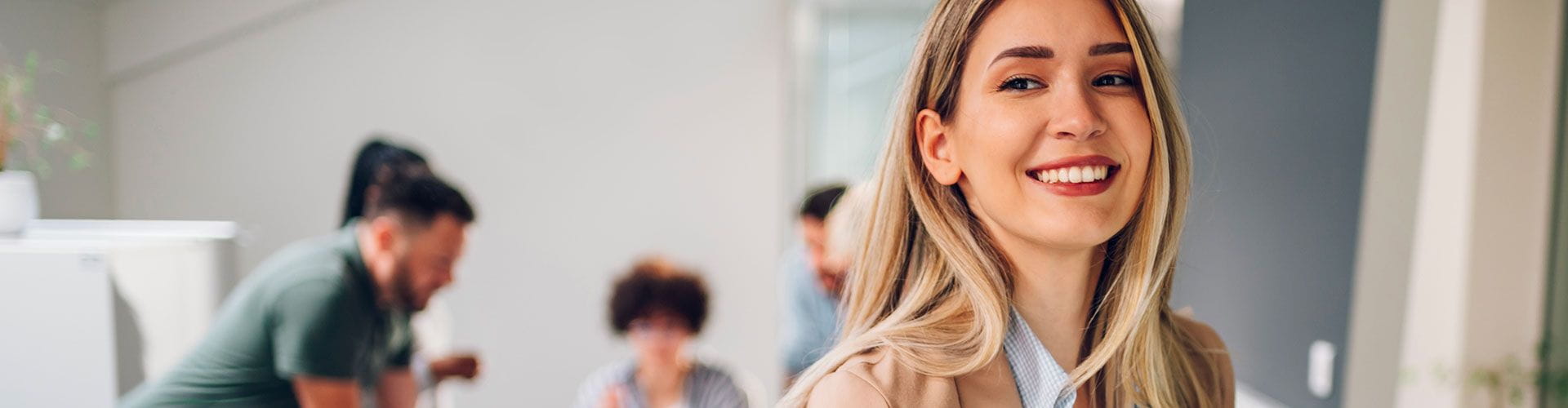 Une jeune femme blonde souriante au premier plan dans un bureau animé