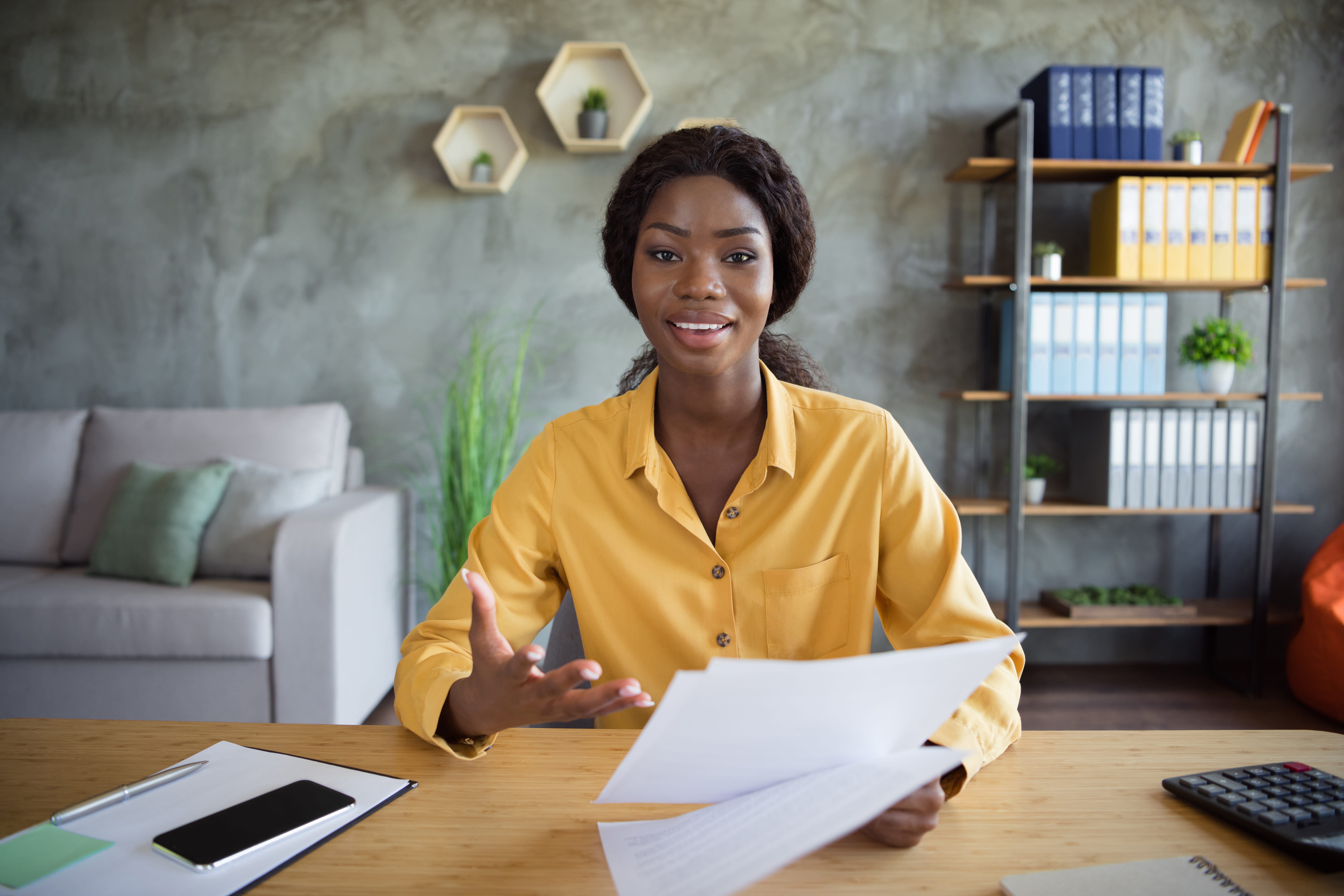 woman wearing yellow shirt seated at desk holding papers in her hand