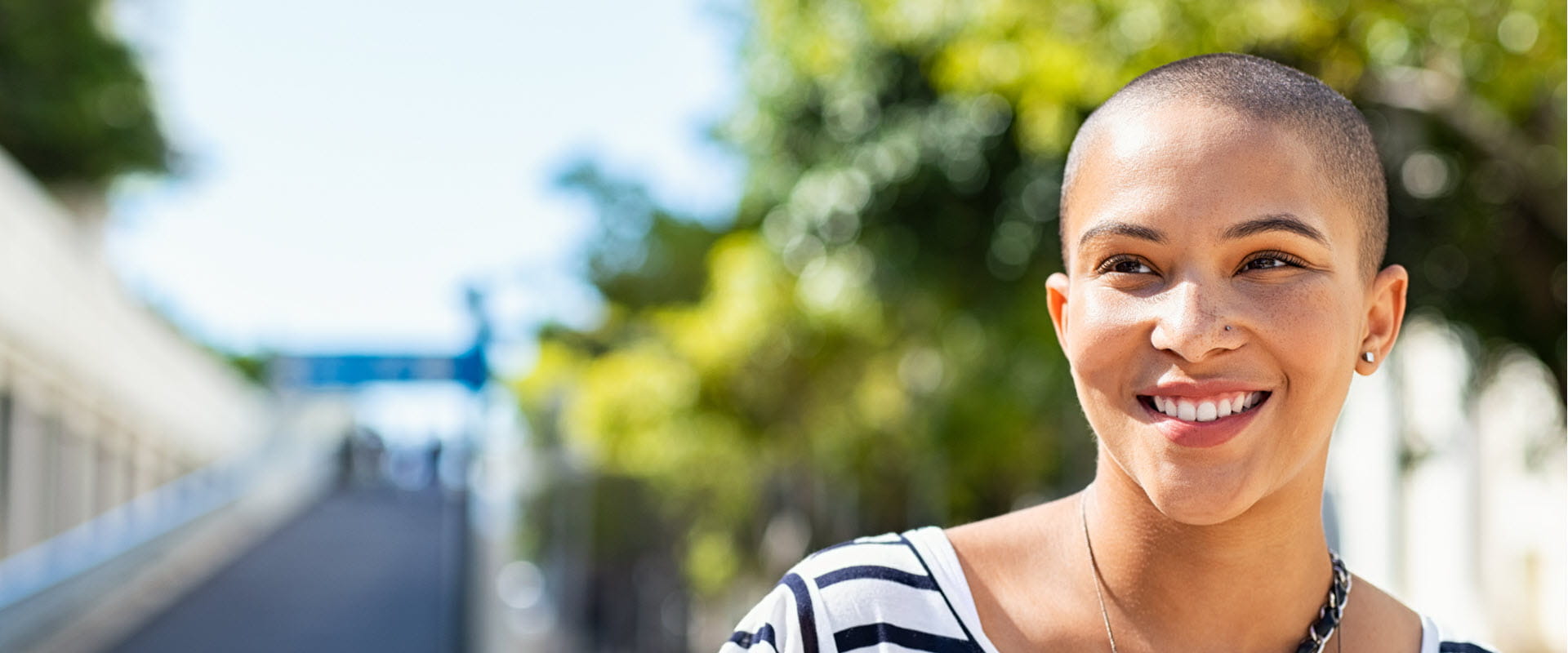 Close-up of a smiling person with short hair and a nose piercing, wearing a striped shirt. 