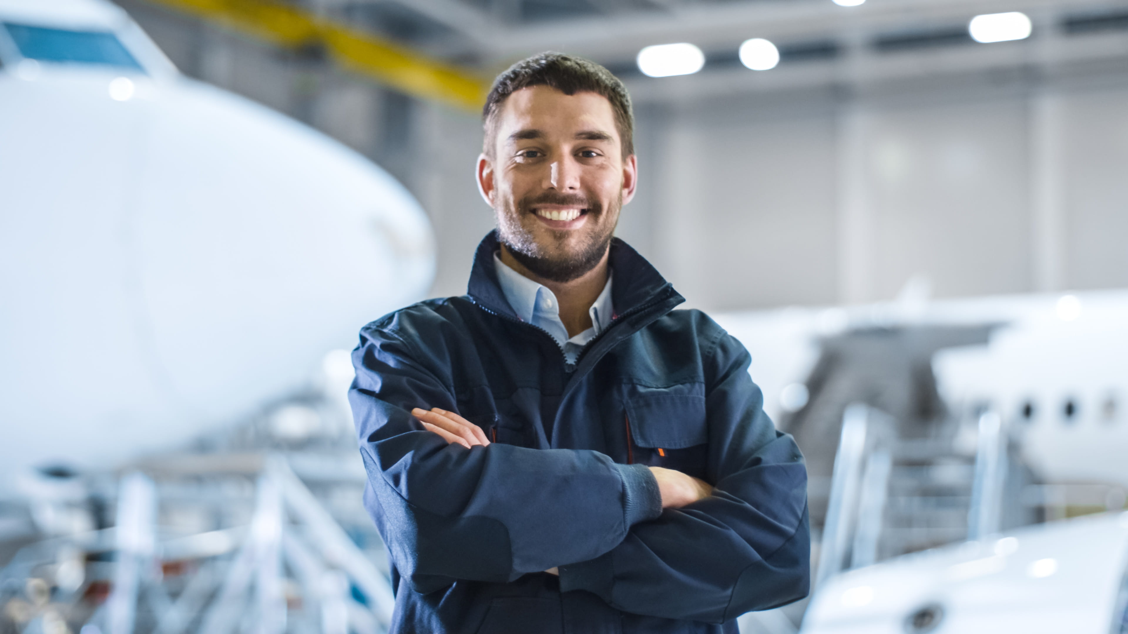 Worker standing with arm crossed in front of airplane in warehouse.