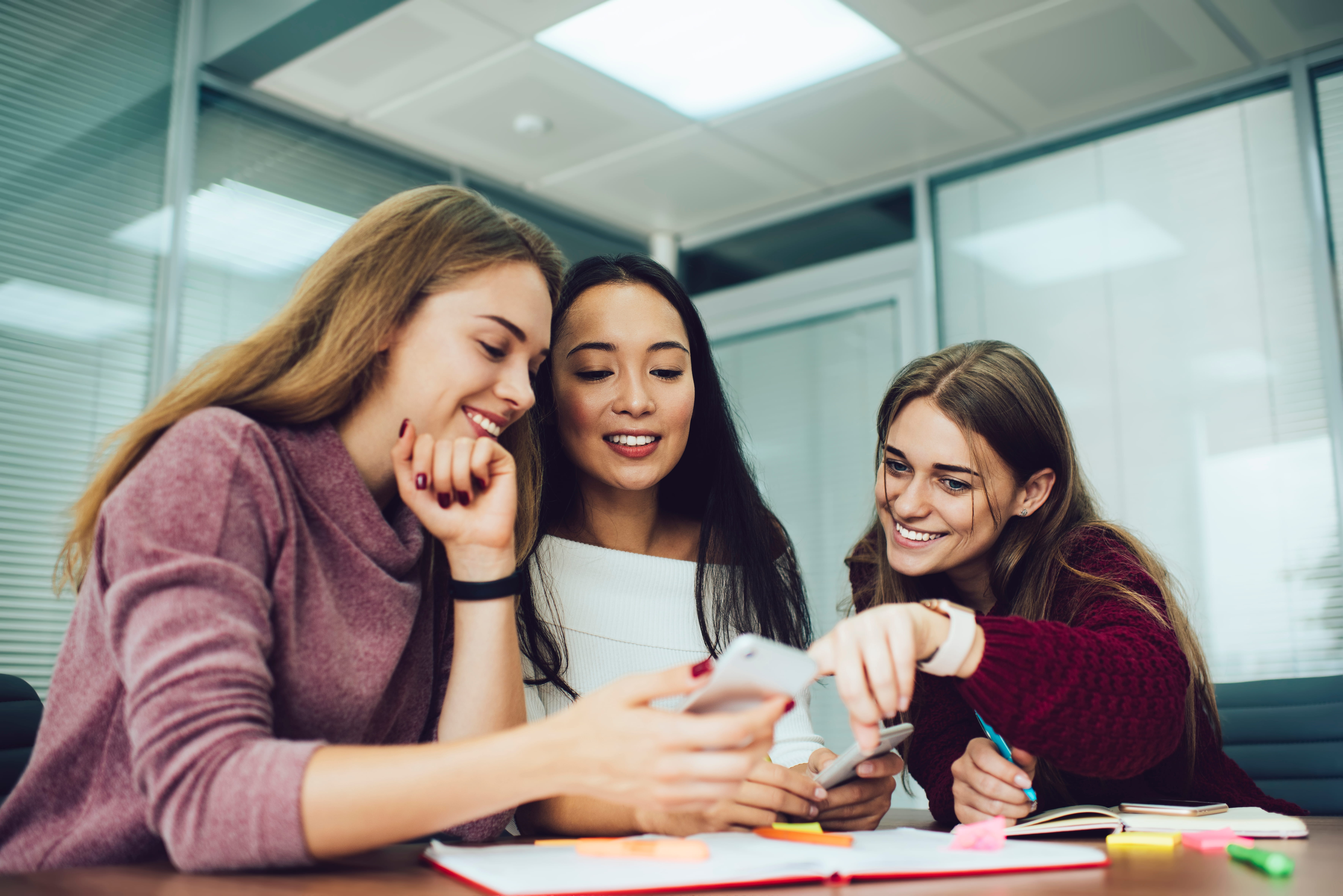 three professional women sitting at table looking at laptop three professional women sitting at table looking at laptop