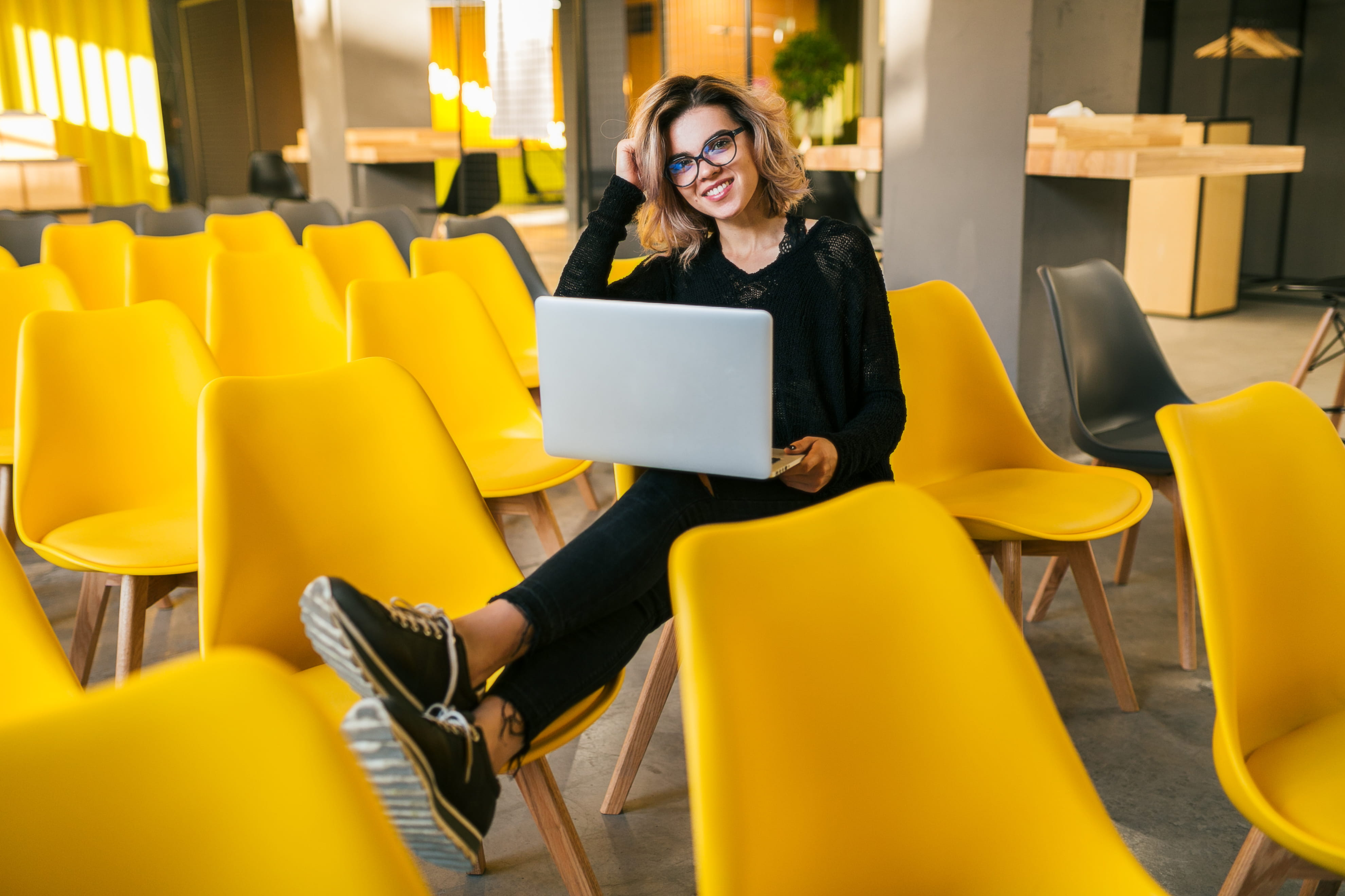 woman sitting on yellow chair holding laptop woman sitting on yellow chair holding laptop