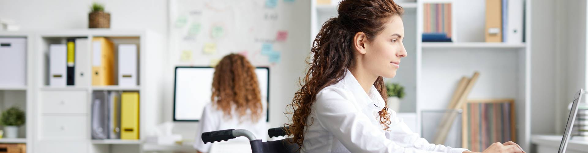 Jeune femme en fauteuil roulant travaillant sur un PC dans un bureau