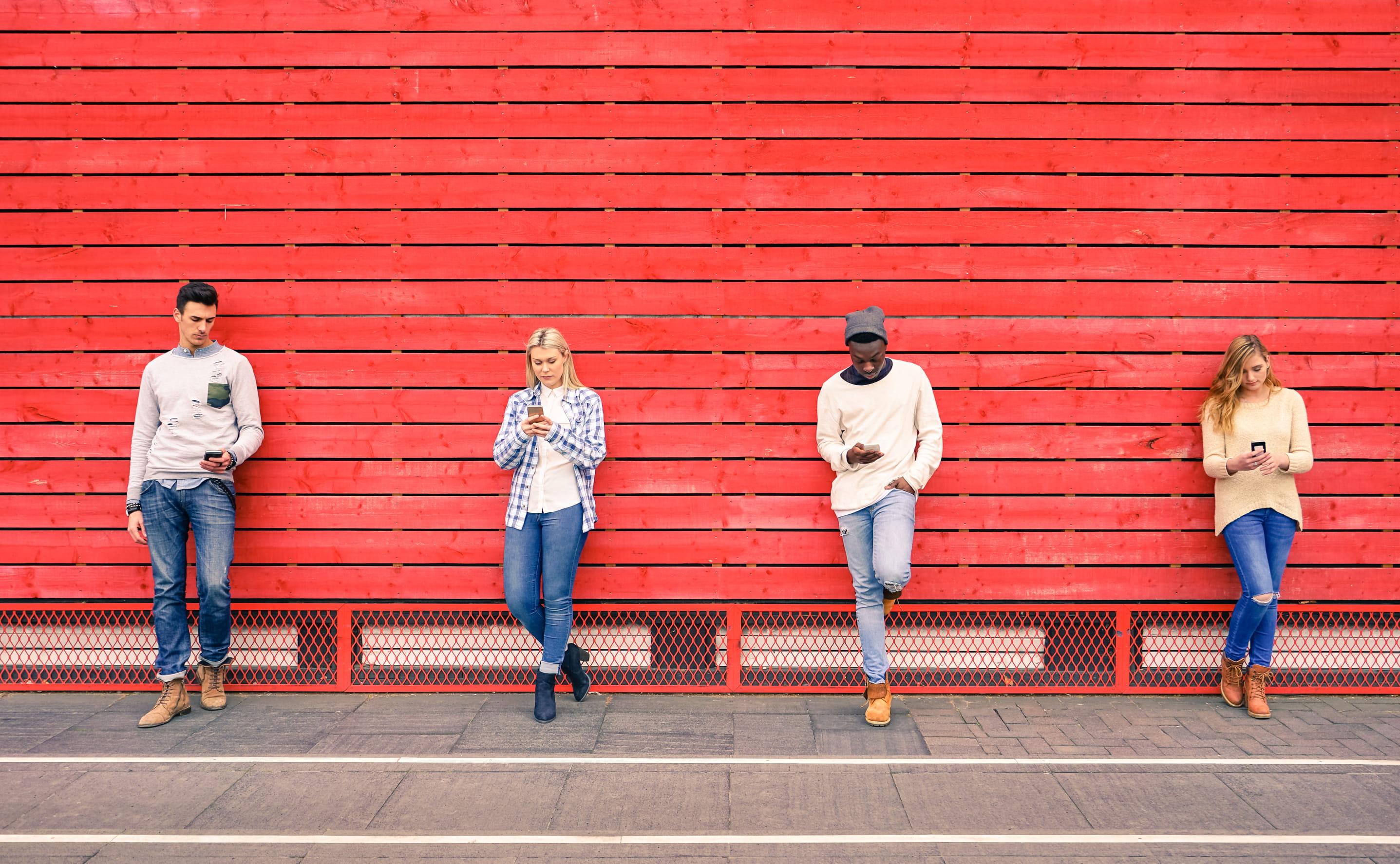 people on their phones leaning against red wall
