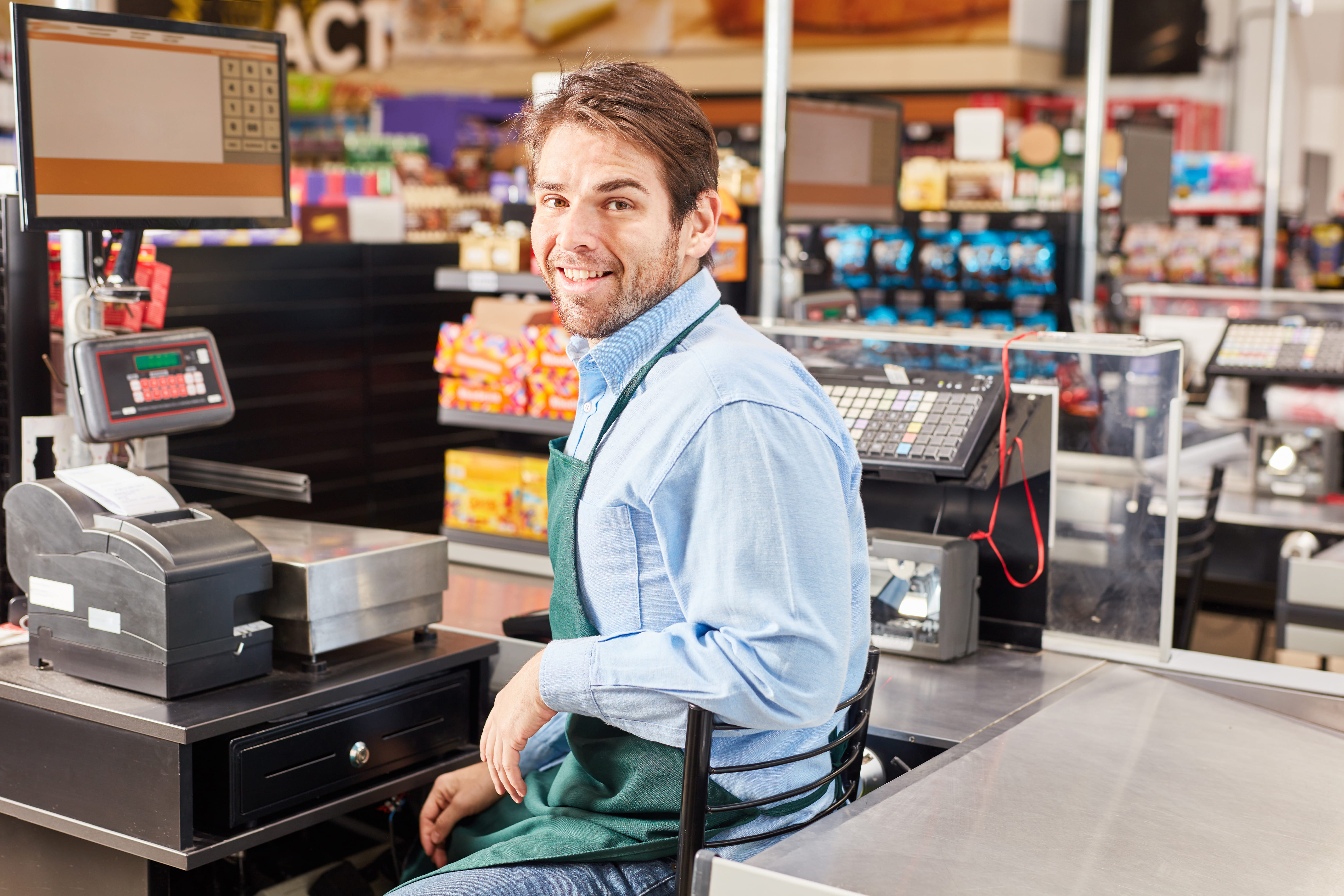 Smiling cashier sits at the cash register in a supermarket.