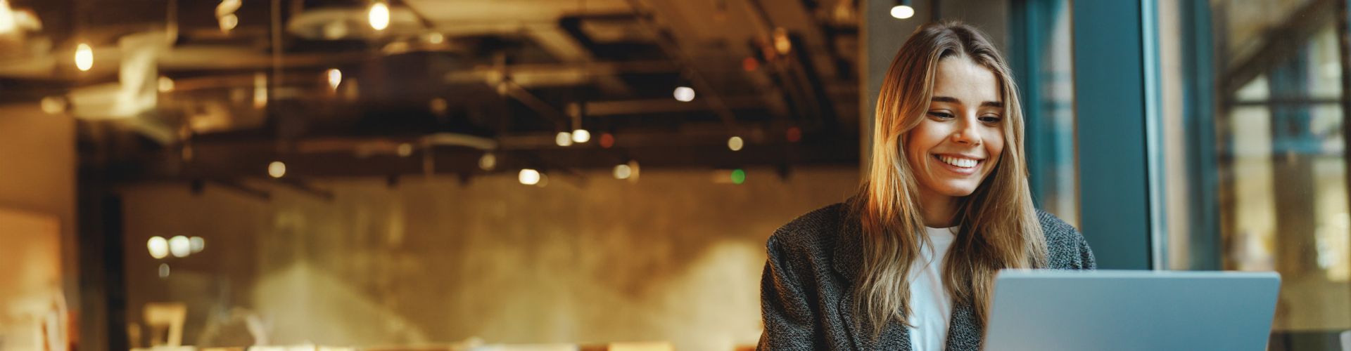 Une jeune femme sourit en regardant son ordinateur.